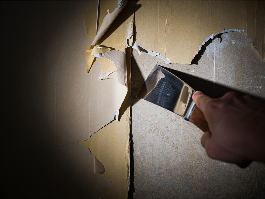 Процесс очистки стены от старой краски и обоев перед нанесением декоративной штукатурки.