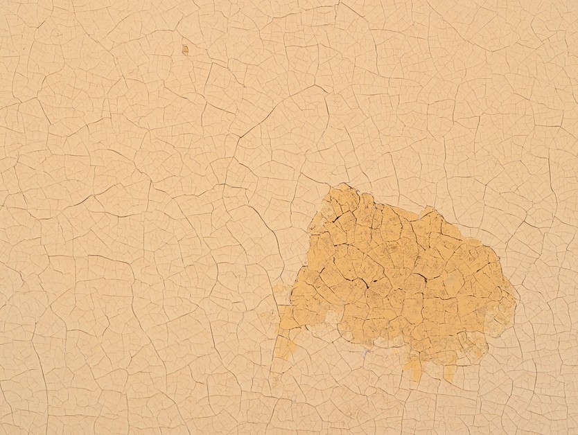 Крупный план стены с потрескавшейся и испачканной дешевой декоративной штукатуркой.